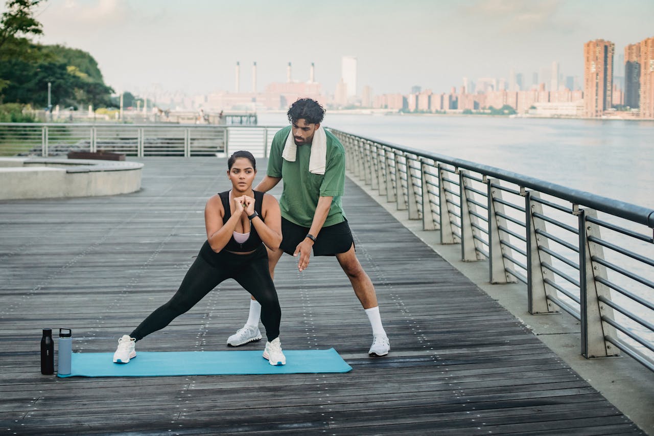 Two adults exercising on a boardwalk with a city skyline in the background.